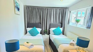 Habitación de hotel con dos camas, cortinas grises, una ventana con vistas y una pequeña planta en el alféizar.