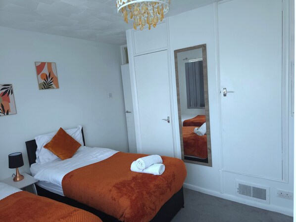 A hotel room with two beds, a large mirror, and a chandelier.