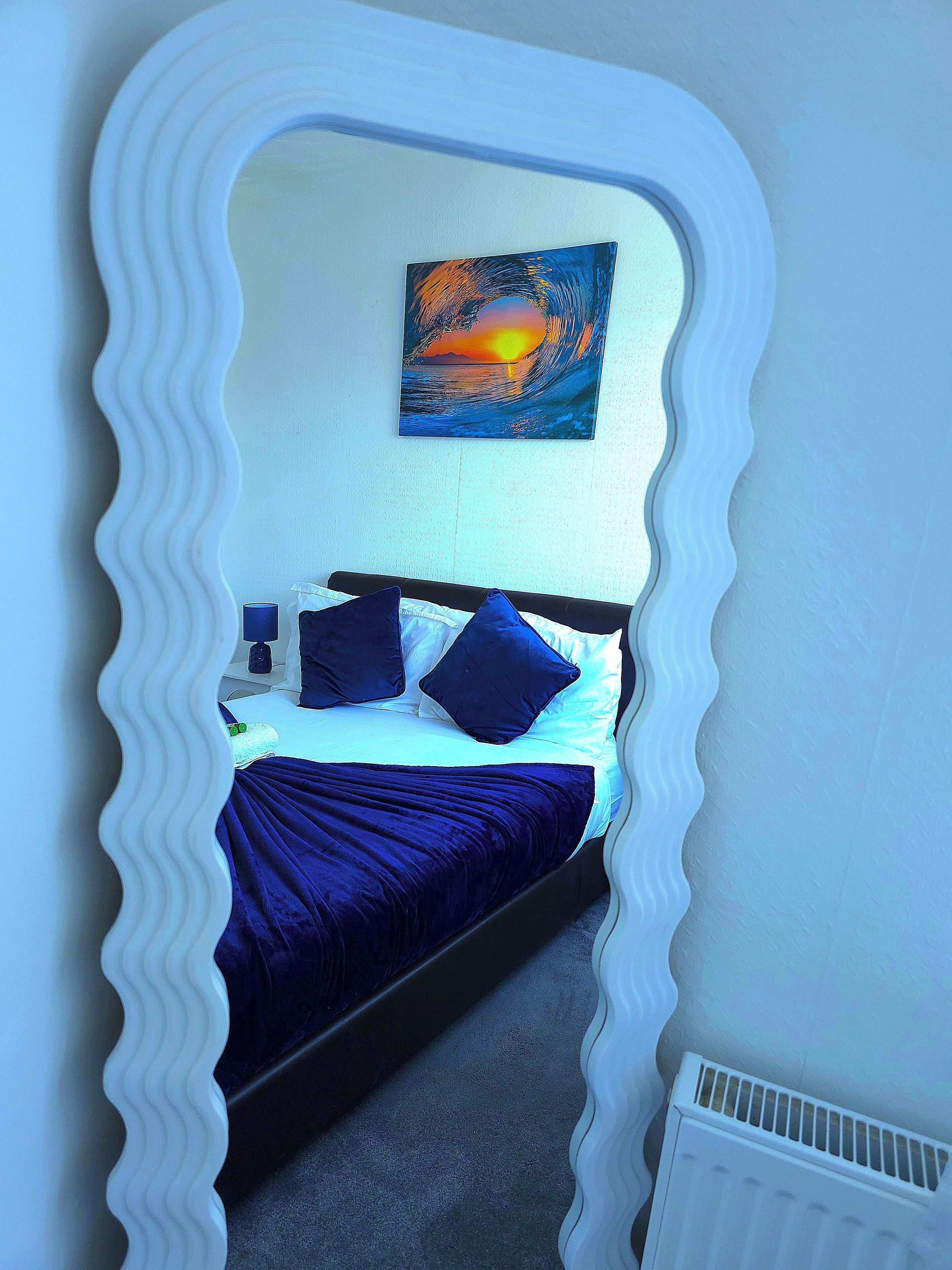 A bedroom with a bed, pillows, a nightstand, and a painting of a sunset.