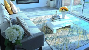 Una sala de estar moderna con un sofá gris, un televisor de pantalla plana, una chimenea, una planta en maceta y vistas al exterior.