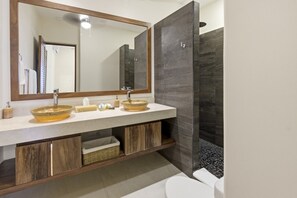 Une salle de bain dotée d’un grand miroir, de deux vasques surmontées de plans-vasques, de toilettes et d’un espace douche.