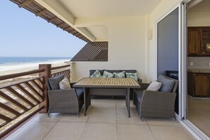 Un balcon avec une table et des chaises, une vue sur la plage et une porte-fenêtre coulissante donnant sur la cuisine.