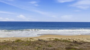 Una spiaggia con onde, cielo sereno e vegetazione rada.