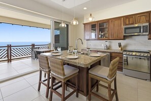 A kitchen with a large island, wooden cabinets, a stove, and a view of the ocean. - 1432 Ocean Front 2 bedroom (Bajos de Chila)