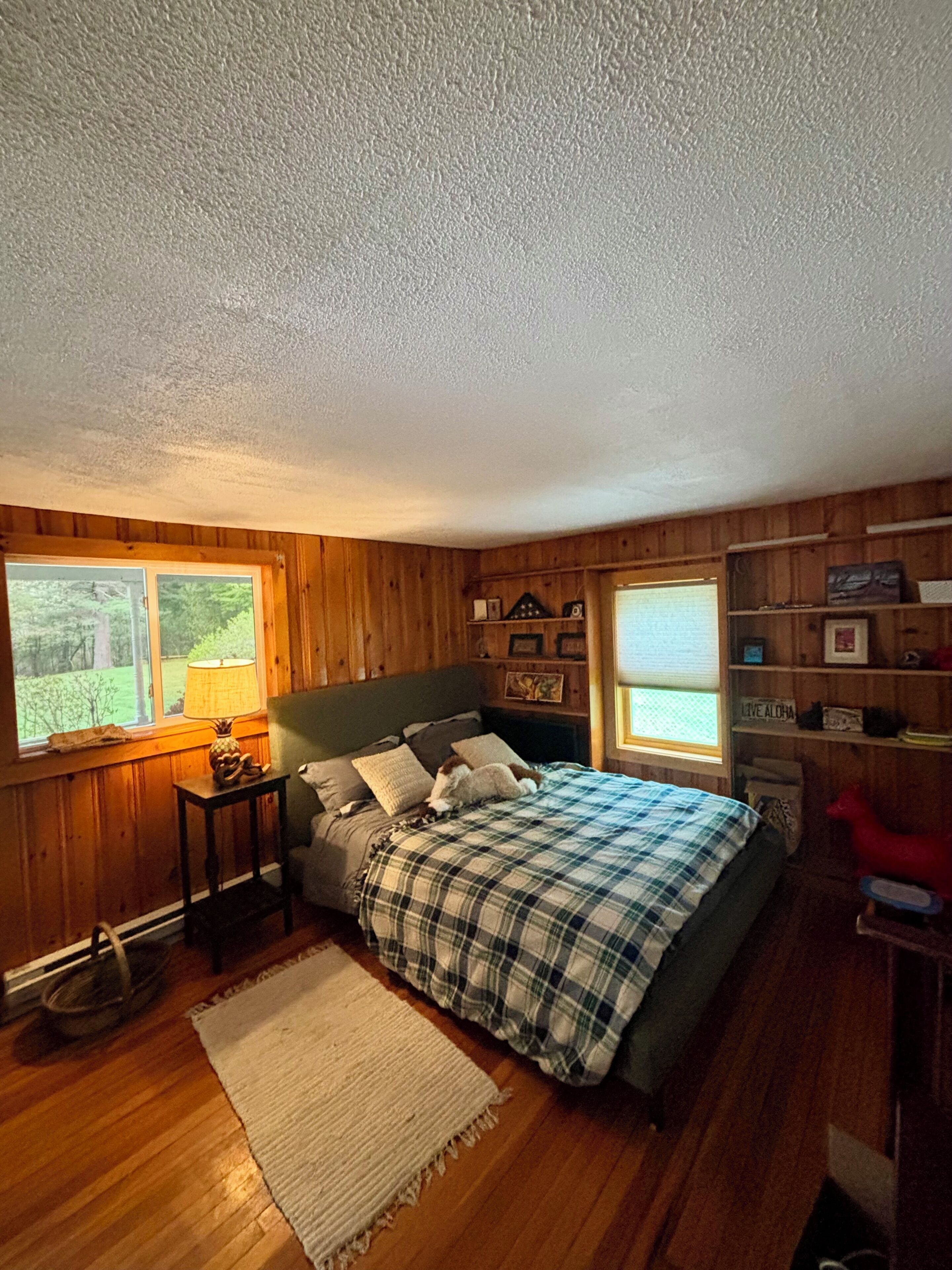 Une chambre à coucher avec un lit, des murs en bois, une fenêtre, une table de chevet et une étagère avec divers objets.