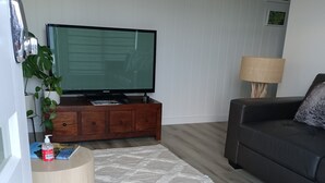A living room with a flat-screen TV on a wooden stand, a dark sofa, a patterned rug, and a wooden floor. - Cosy 1 Bedroom Unit with separate living space, laundry and kitchen. (Prospect Vale)