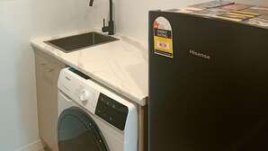 A compact kitchen with a washing machine, a sink, and a refrigerator. - Cosy 1 Bedroom Unit with separate living space, laundry and kitchen. (Prospect Vale)