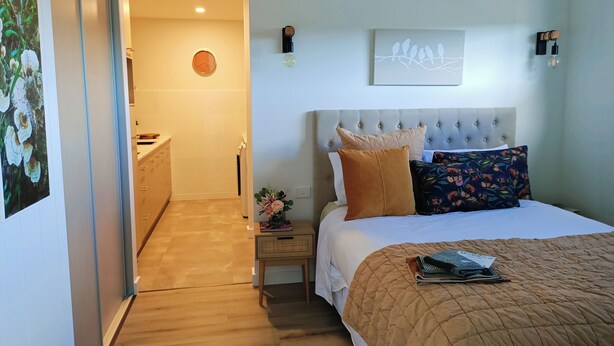 A bedroom with a bed, a nightstand, a wall clock, and a painting. - Cosy 1 Bedroom Unit with separate living space, laundry and kitchen. (Prospect Vale)