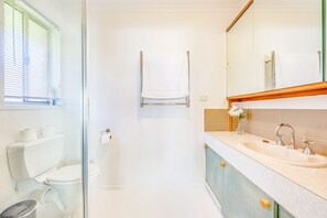 Un baño moderno con cabina de ducha de vidrio, inodoro blanco, lavamanos con espejo y toalla colgada en un perchero.