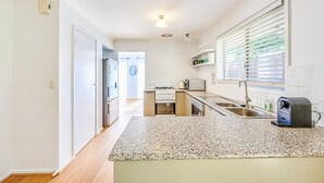 A modern kitchen with granite countertops, white cabinetry, and a built-in oven. - StayAU Family-Friendly Home near Deakin (Whittington)