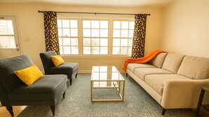 Ein Wohnzimmer mit einem grauen Sofa, einem beigen Sofa und einem Glastisch.