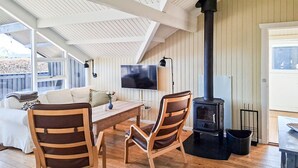 A cozy room with a wooden table, two chairs, a sofa, a TV, and a wood-burning stove. - 3 bedroom nice home in Haarby (Haarby)