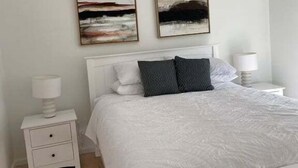 Een slaapkamer met een wit bed, twee nachtkastjes en twee abstracte schilderijen aan de muur.