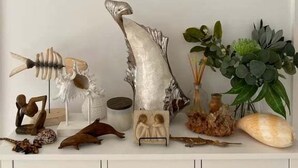 Een witte dressoir met een lijstfoto van een strand, diverse decoratieve items waaronder een viskarkas, schelpen en een potplant.
