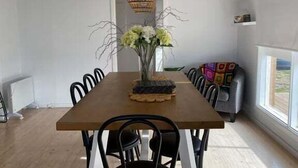 Een eetruimte met een houten tafel, zwarte stoelen, een vaas met bloemen en een hanglamp.