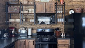 A kitchen with wooden cabinets, a stove, a microwave, and shelves with various kitchen items.