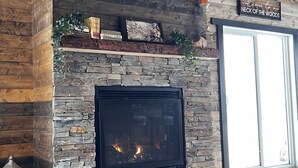 A modern living room with a stone fireplace, a flat-screen TV mounted above it, and a sign reading "Welcome to our NECK OF THE WOODS."