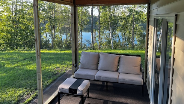 A covered porch with a sofa and ottoman, a view of a lake, and a grassy area.