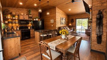 A rustic cabin interior with a wooden dining area, kitchen, and living space.