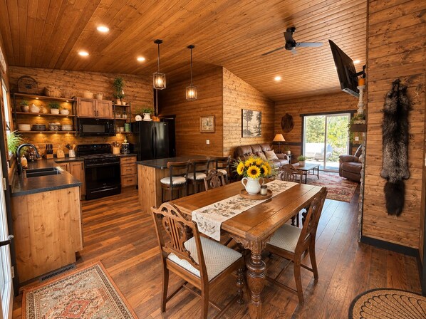 Interior rústico de una cabaña con comedor de madera, cocina y sala de estar.