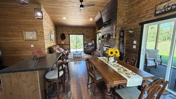 A wooden interior with a dining area, a fireplace, and a sign reading 'Welcome to the Neck of the Woods.'