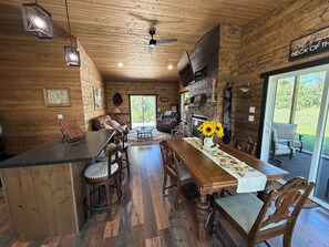 Interior de madera con comedor, chimenea y un letrero que dice 'Welcome to the Neck of the Woods'.