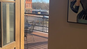 Udsigt fra en balkon med et bord og stole, en rød murstensbygning i baggrunden og et billede i ramme på væggen.