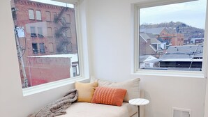 Una habitación moderna con sofá cama, dos ventanas y vistas a edificios.