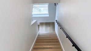 Una escalera de madera con barandilla negra que conduce a un rellano con ventana.