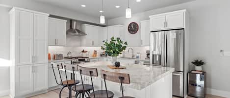 A modern kitchen with white cabinets, a central island with bar stools, stainless steel appliances, and pendant lighting.