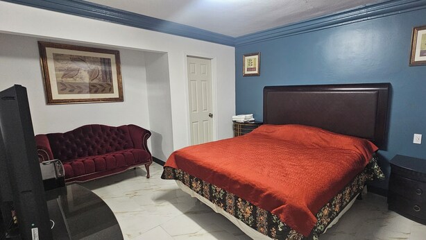 A bedroom with a bed, a red sofa, a television, and a door.