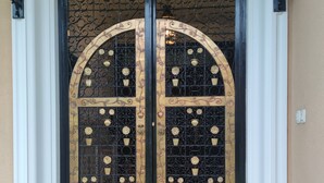 A double door with intricate metalwork and floral designs, flanked by two wall-mounted lanterns. - Rural house in the heart of De la Vera in Yuste, Imperial retreat (Cuacos de Yuste)
