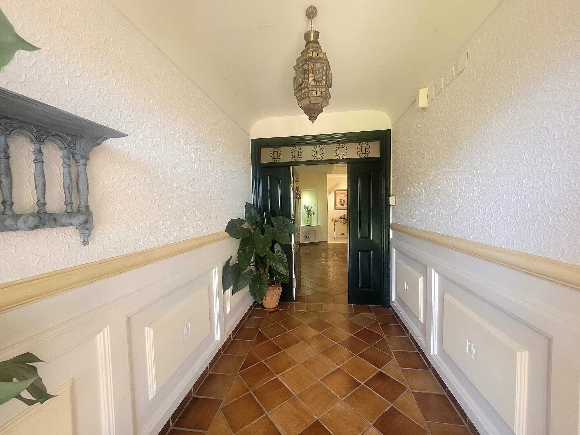 A hallway with patterned walls, a tiled floor, and a hanging light fixture.