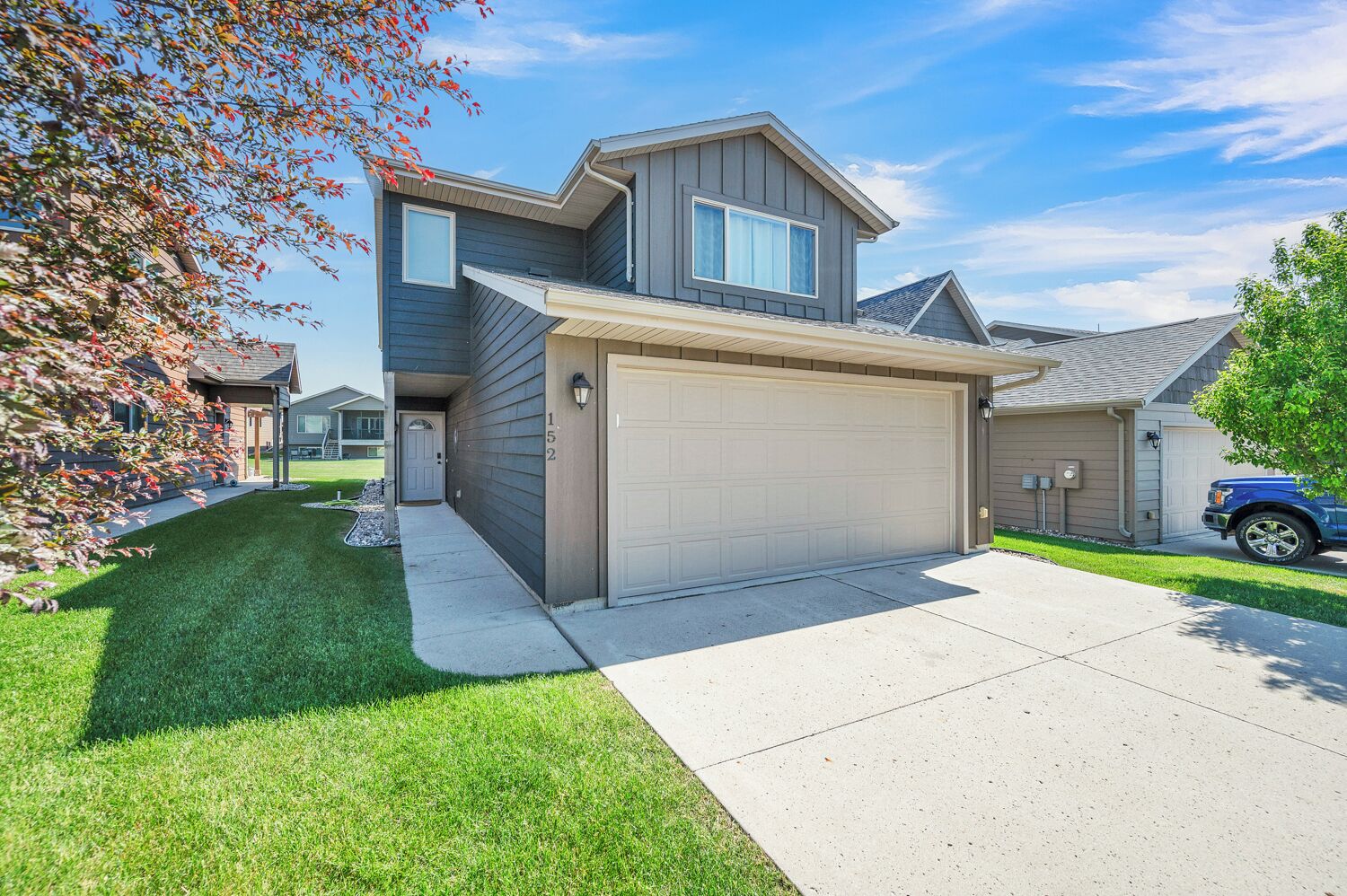 A modern two-story house with a garage, a well-maintained lawn, and a clear sky.