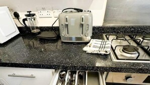 Una cocina con mostrador negro, un tostador y un organizador de cajones con utensilios.