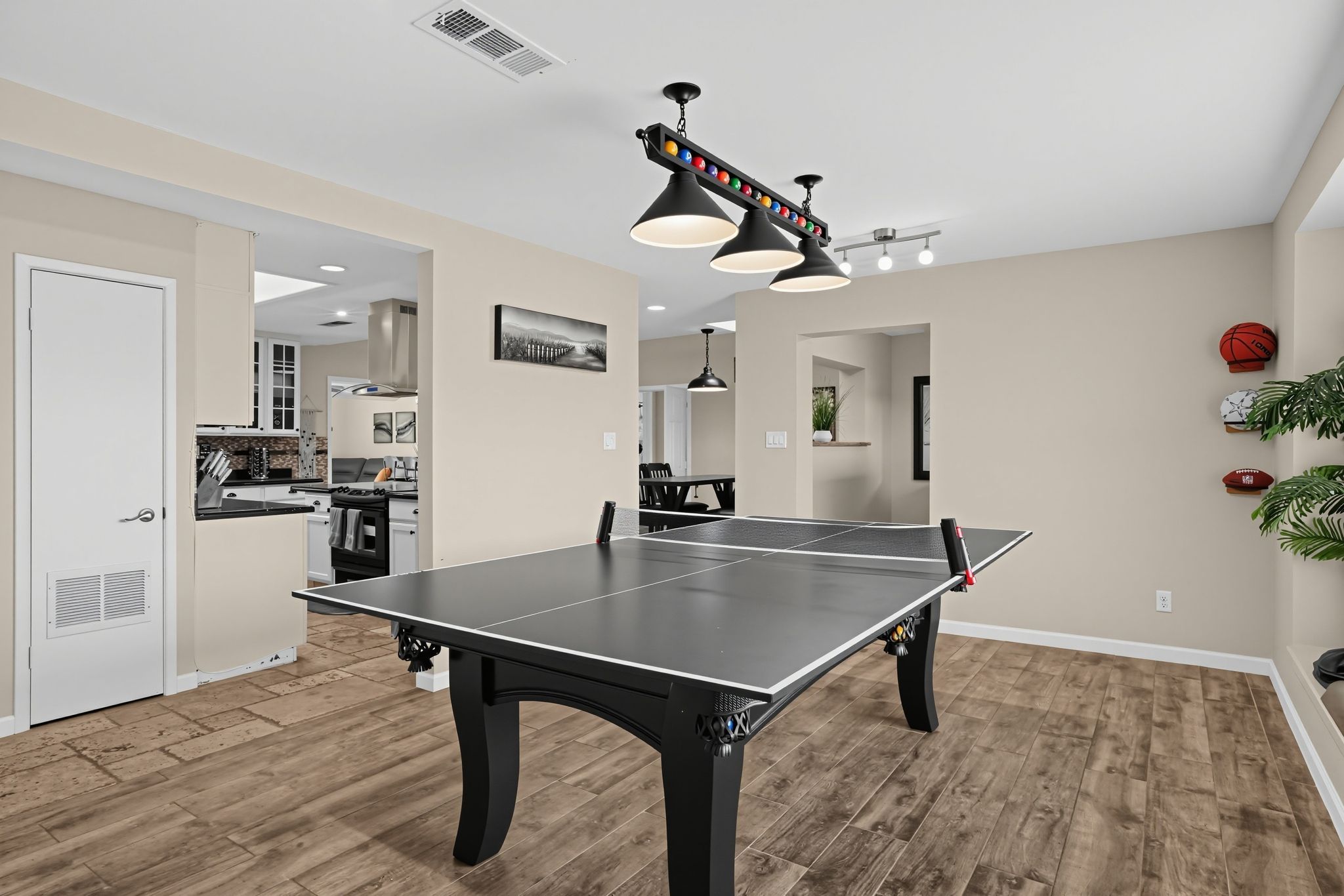 A ping pong table in a room with wooden flooring, a kitchen in the background, and a ceiling fan.