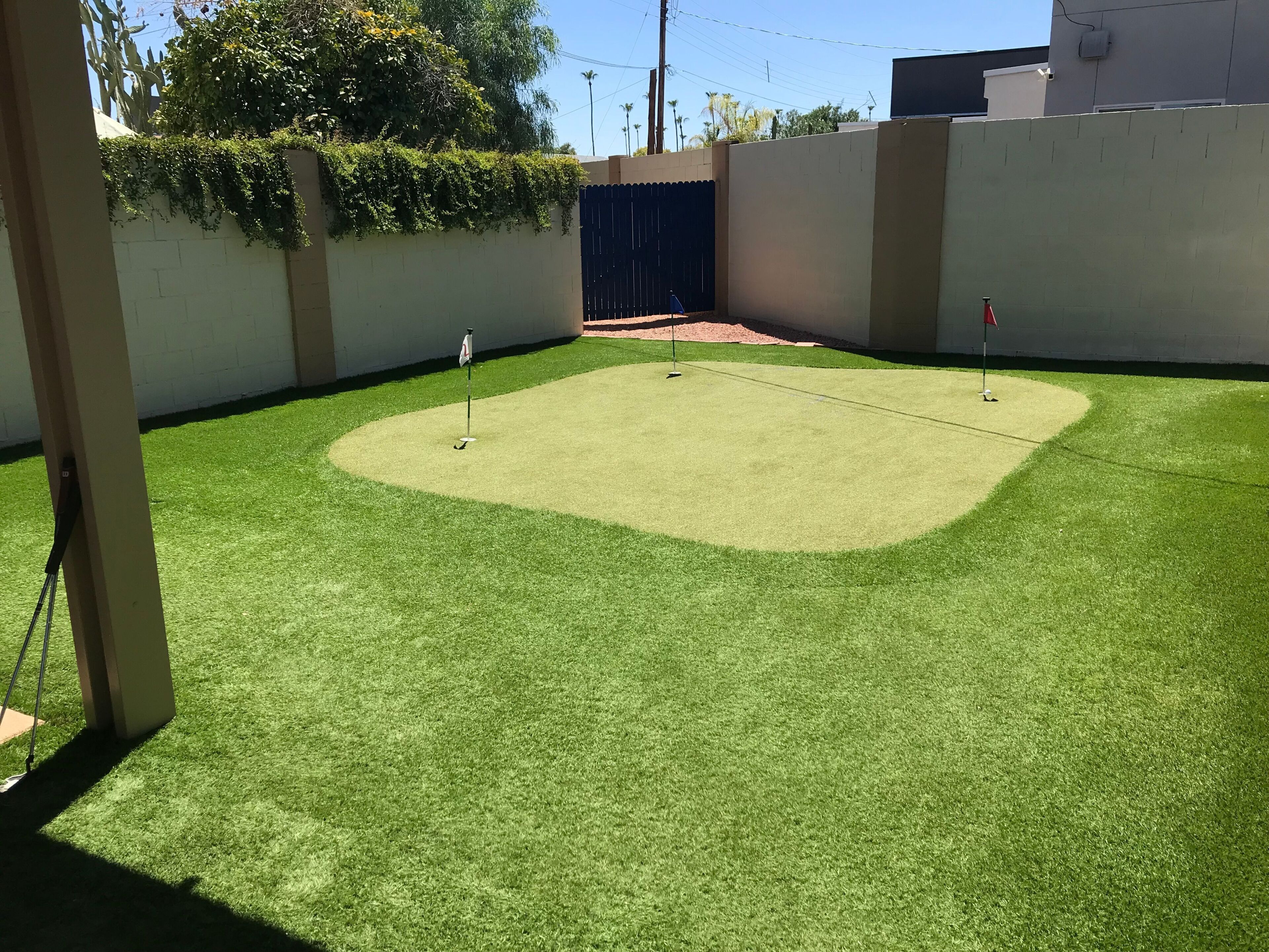 Een verzorgd grasveld van kunstgras met een vlaggenmast en golfbal, omringd door muren en een poort.
