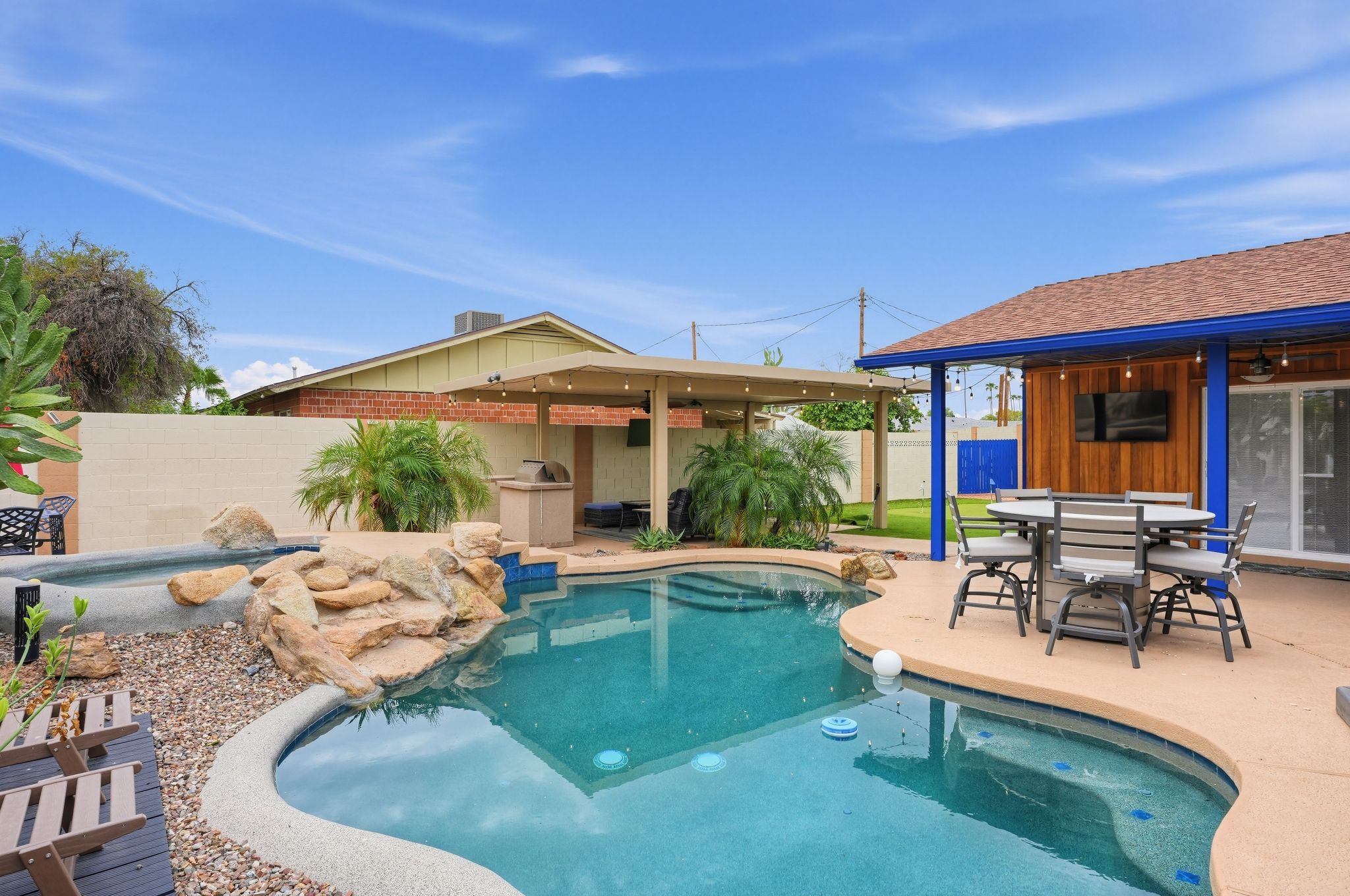 A backyard with a swimming pool, a covered patio, and a barbecue area.