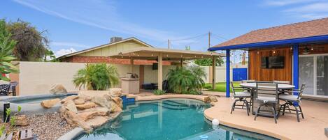 A backyard with a swimming pool, a covered patio, and a barbecue area.
