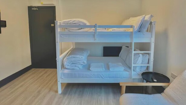 A bunk bed room with a wooden floor, a small table, and a door in the background. - Golder Greens London City Bliss Apartment (London)