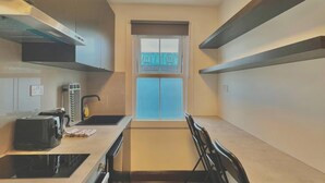 A compact kitchen with a built-in stove, a coffee maker, and a window with a view of the city. - Golder Greens London City Bliss Apartment (London)