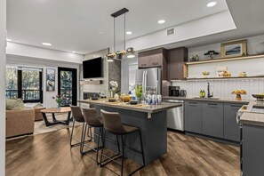 A modern kitchen with a central island, bar stools, and a large window overlooking a balcony. - Apres Hydeaway at Ascent (Canmore)