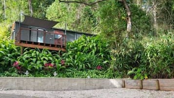 Een houten chalet met balkon, omringd door weelderige begroeiing en bomen.