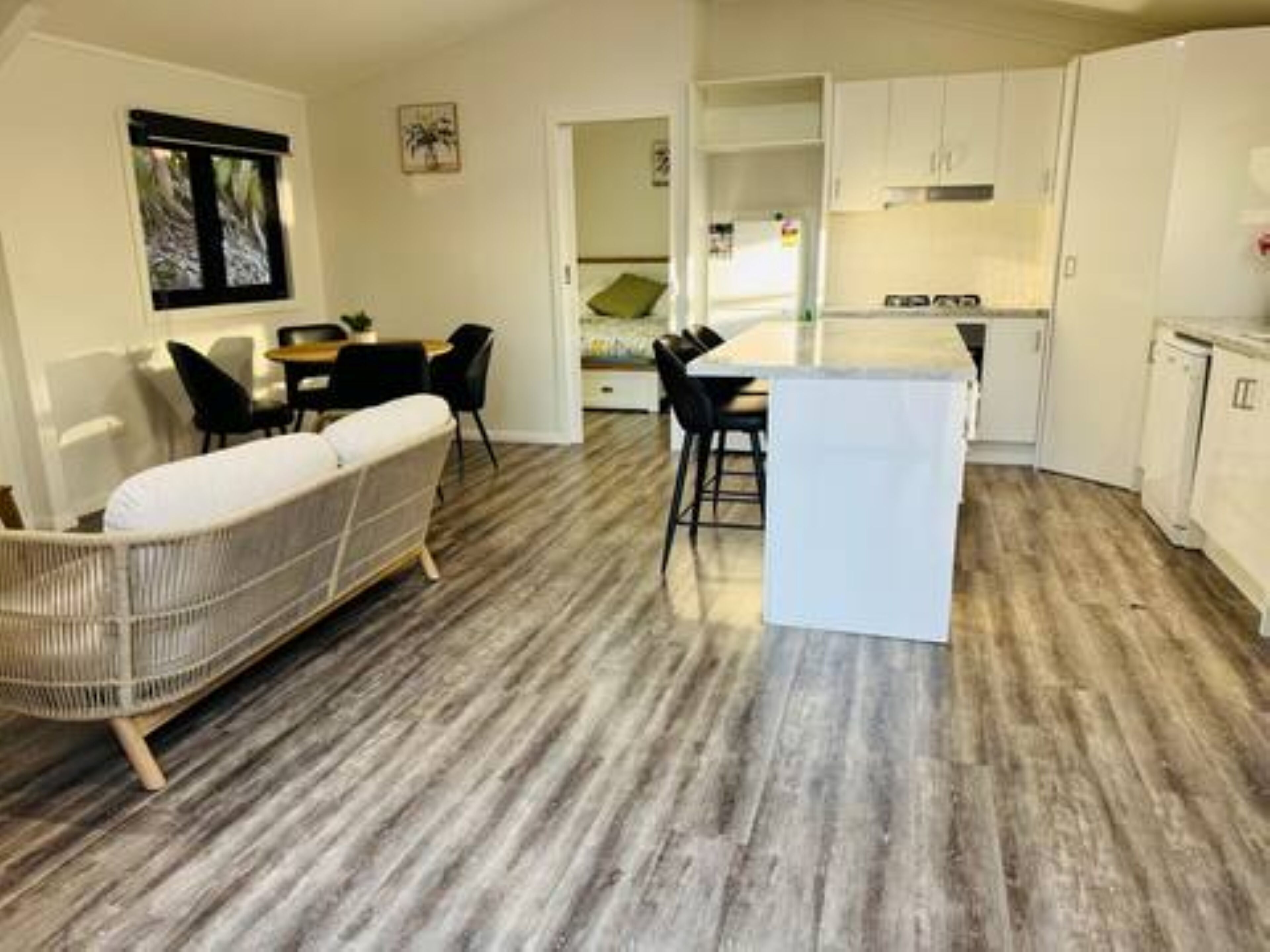 A modern kitchen with white cabinets, a dining area with a white sofa and black chairs, and a wooden floor.