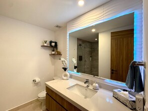 Een moderne badkamer met een wit wastafelmeubel, een grote spiegel en een douchehoek.