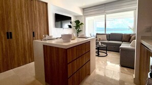 A modern living room with a large window, a sofa, and a coffee table. - Oceanview 1BR w/ Breakfast | Rooftop Pool & Gym (Puerto Vallarta)