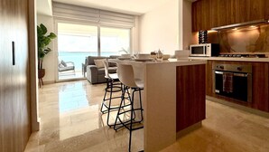 A modern kitchen with a central island, bar stools, a microwave, and an oven. - Oceanview 1BR w/ Breakfast | Rooftop Pool & Gym (Puerto Vallarta)
