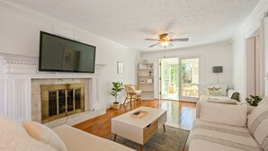 A living room with a fireplace, a television, a ceiling fan, and a view to the outside. - 1223 Settlebench Ln NW Kennesaw (Kennesaw)