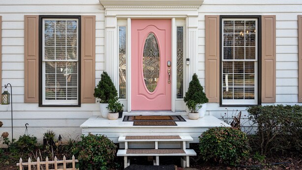 A house with a pink door, two potted plants, a bench, and a white porch. - 1223 Settlebench Ln NW Kennesaw (Kennesaw)