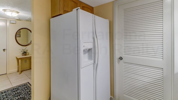 A kitchen with a white refrigerator, wooden cabinets, a small console table with a plant, and a white door with horizontal slats. - 2063 Beachwood Lovely 2 Bedroom, 2 Bath Beach Wood Villa is Located in Amelia Island Plantation Resort (Fernandina Beach)